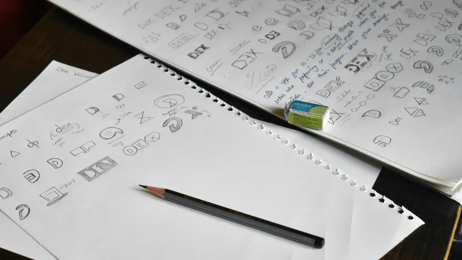 Pages of hand-drawn logo design sketches and concepts with a pencil